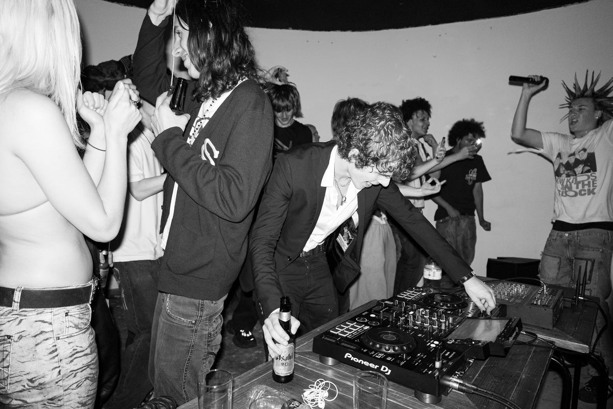 A crowd at a London party, shot on direct flash. A DJ over the decks, drinks up, nobody posing.